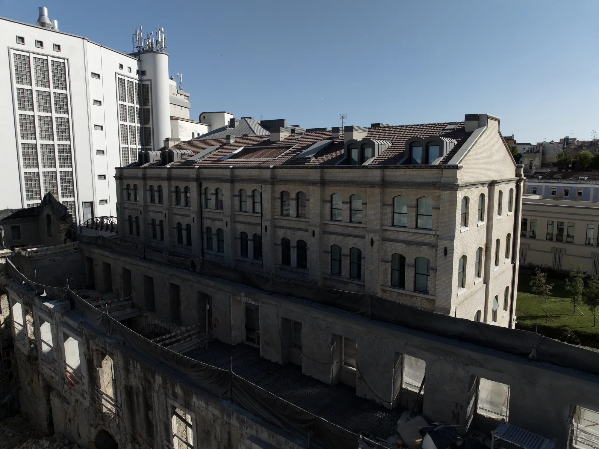 Old stone walls and arches without a roof, in front of the pale restored building with its dormers.