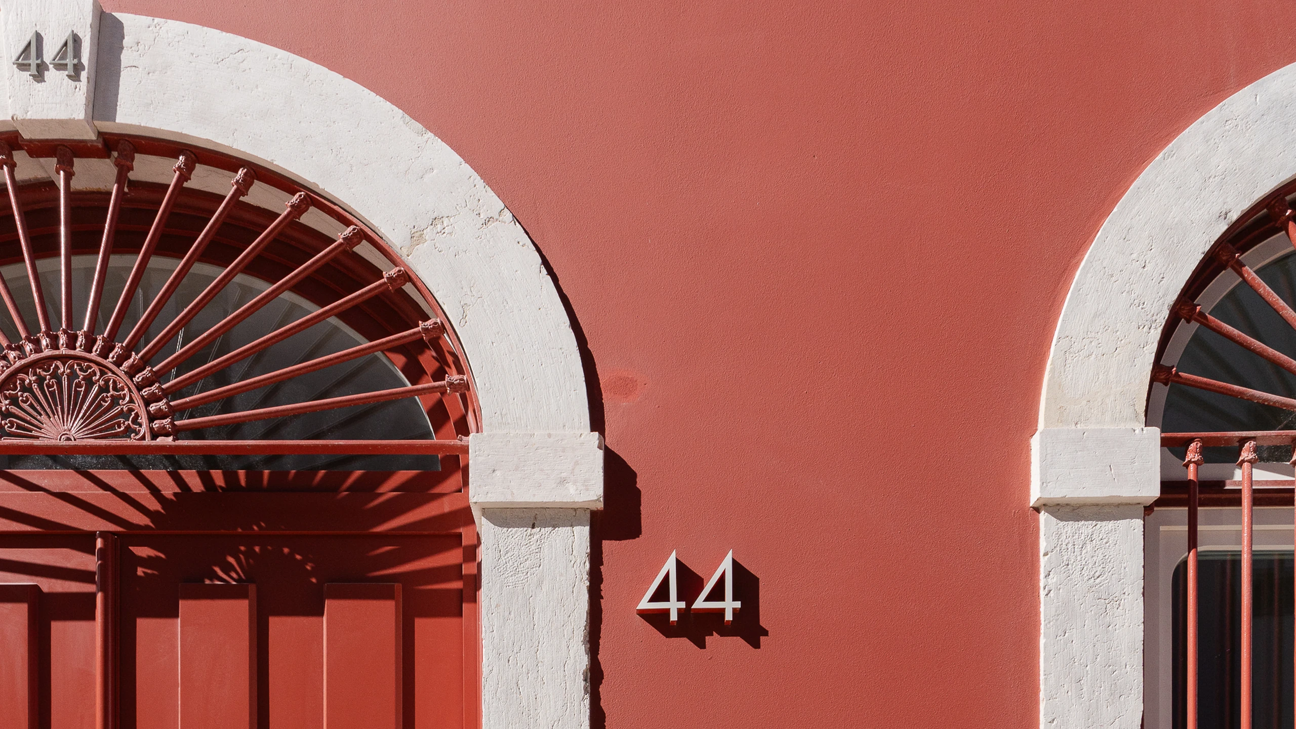 Door 44 of Moagem: a white stone arch over a red iron fanlight on the red wall.