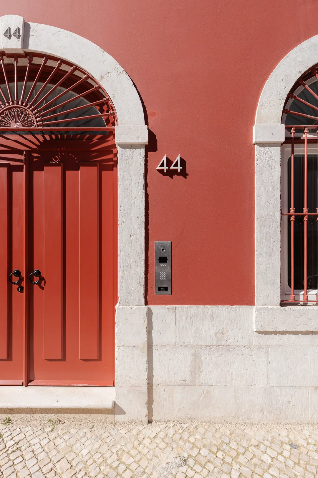 The door at Rua do Beato 44: a red panelled double door under a stone arch with a fanlight, on cobbled pavement.