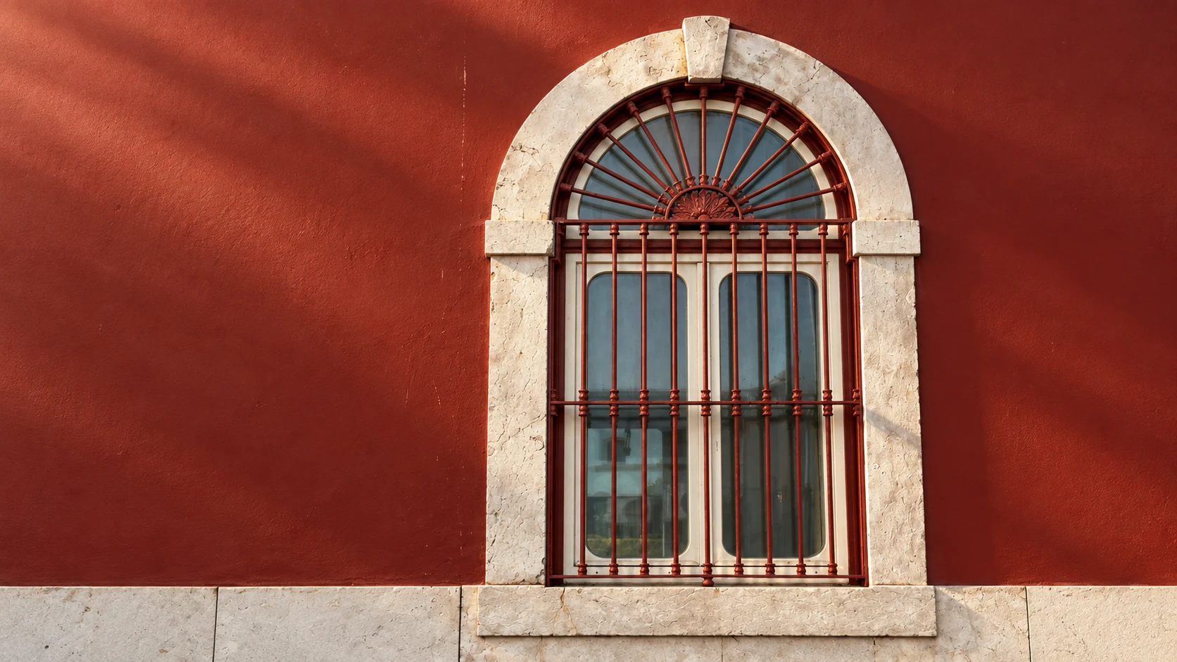 Visual study of the arched window: a red iron fanlight, pale stone and grazing light.