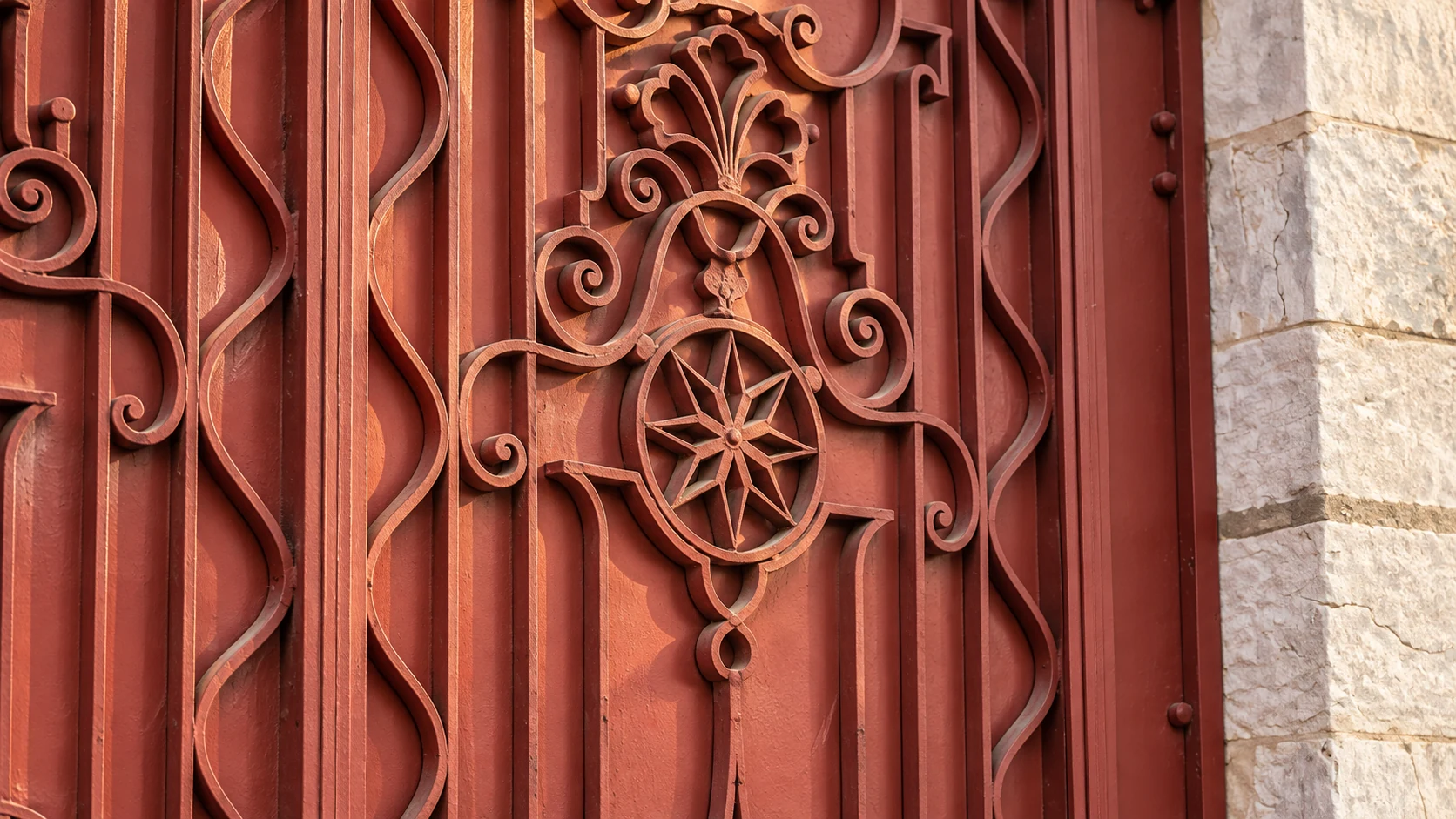 Visual study of a red gate in the quarter, with a star rosette and botanical ironwork.