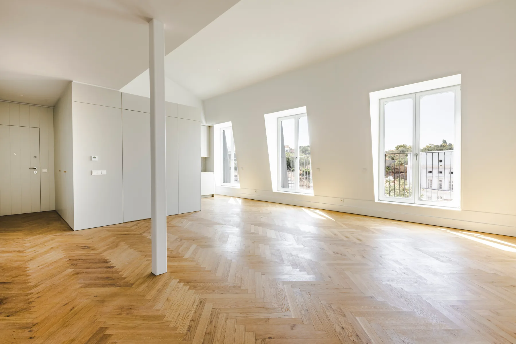 The living room towards the doors: the white column, a door and white built-in units at the far end, and tall white-framed windows along the right wall.