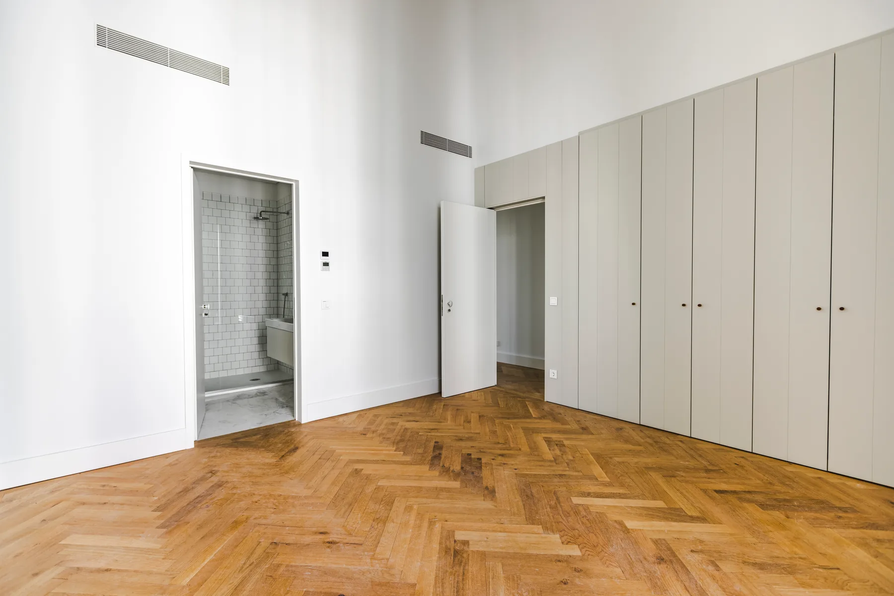 The same bedroom towards the doors: a wall of built-in wardrobes, the open door to a bathroom and the door to the corridor.