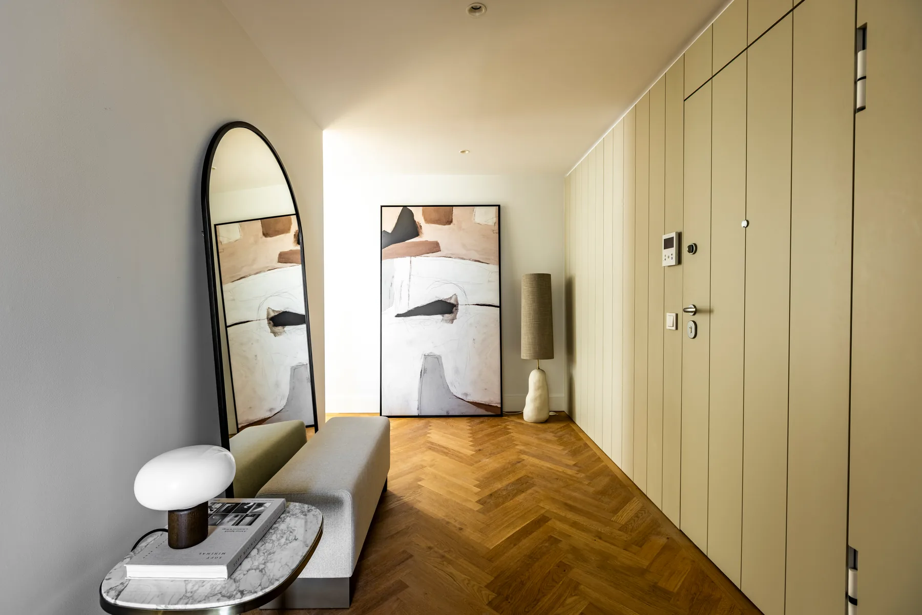 The hall: full-height built-in cupboards and a door with an intercom panel on one side, an arched mirror, a bench and a small side table on the other.