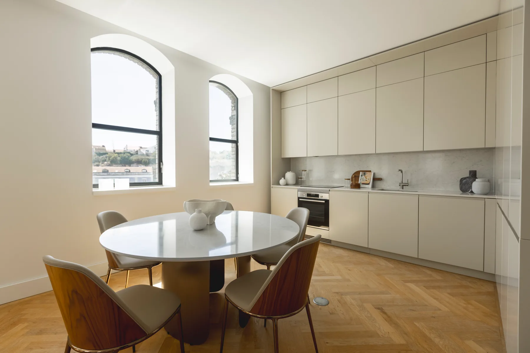 The kitchen along one wall, with a round dining table and four chairs under two arched windows.