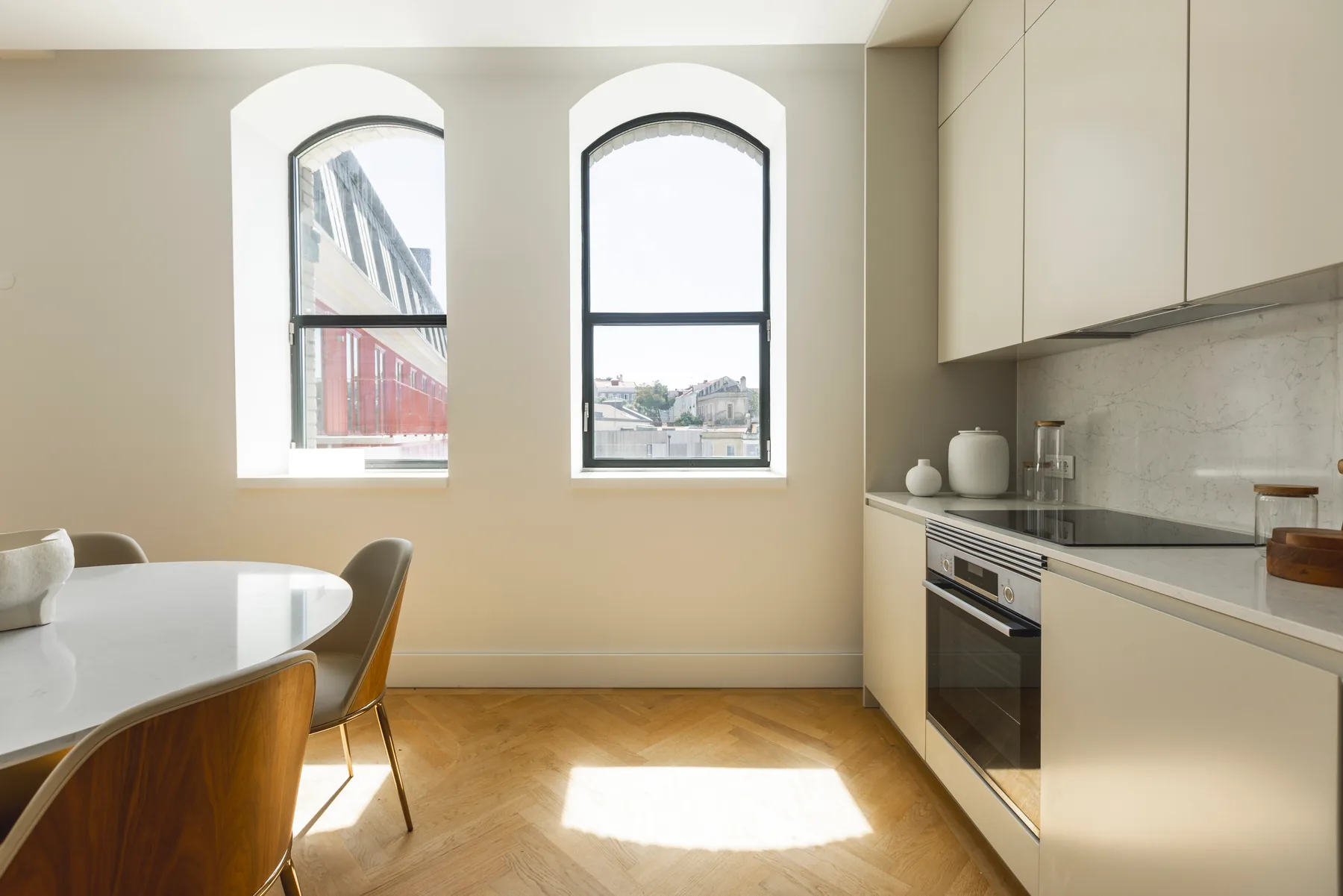 The kitchen counter with a built-in oven and hob, running up to two arched windows beside the round dining table.