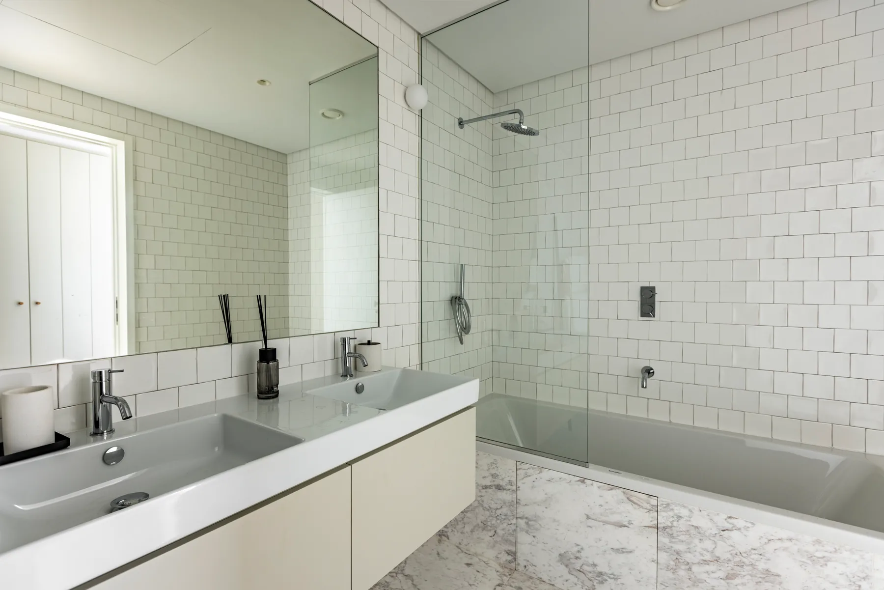 The same bathroom from the basin: a long white vanity, a wide mirror and the glass shower beside it.