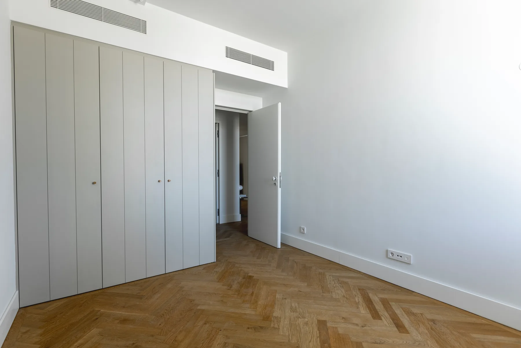 The same bedroom towards the door: a long wall of built-in wardrobes and the open door.