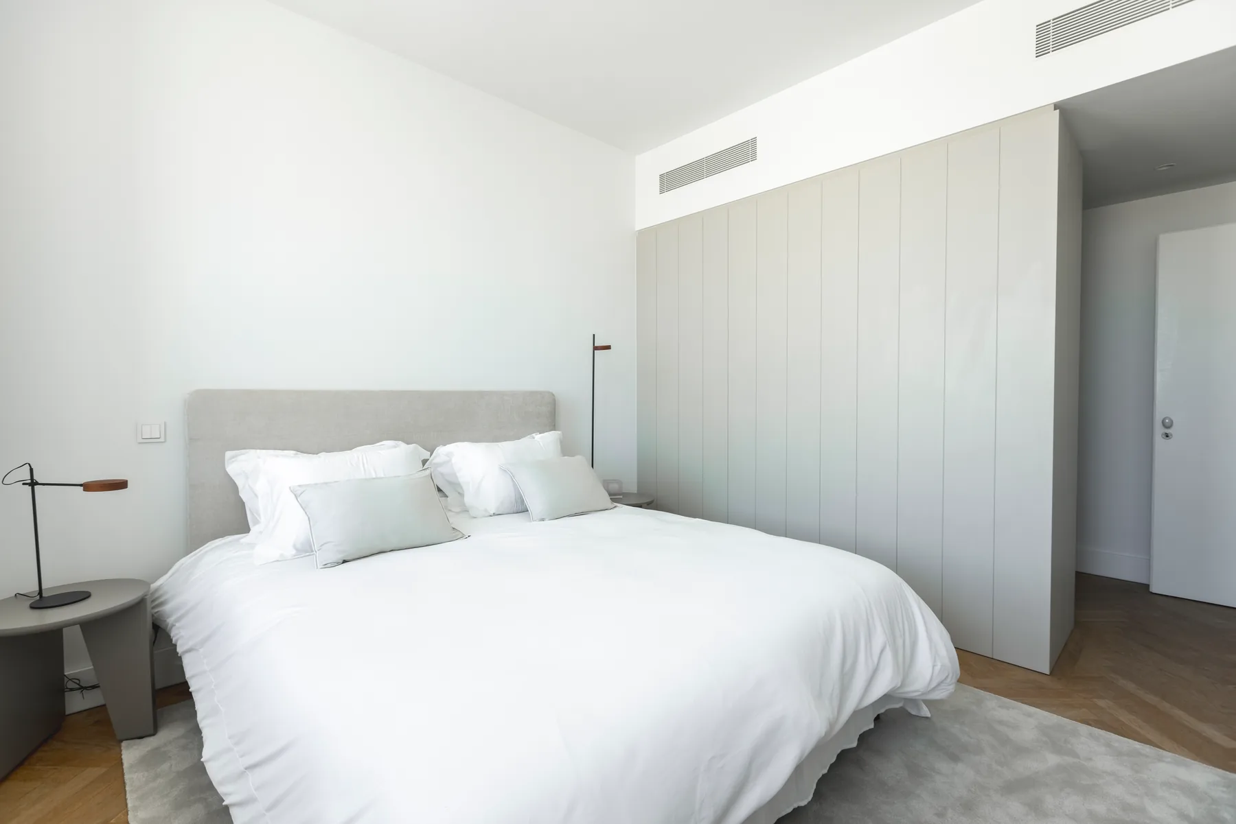 The staged bedroom towards the door: the double bed, a bedside table and a wall of built-in wardrobes.
